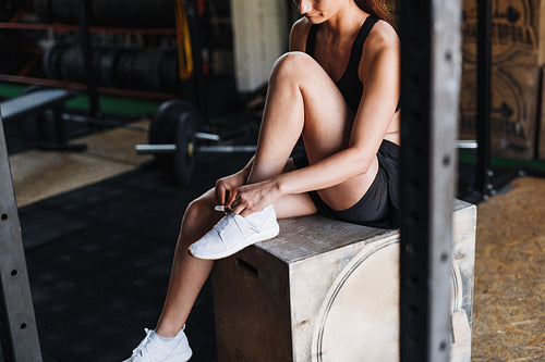 Unrecognizable woman sitting in gym tying shoelaces on sneakers