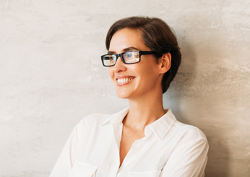 Cheerful businesswoman wearing eyeglasses. Portrait of a smiling entrepreneur leaning against a wall wearing formal wear.