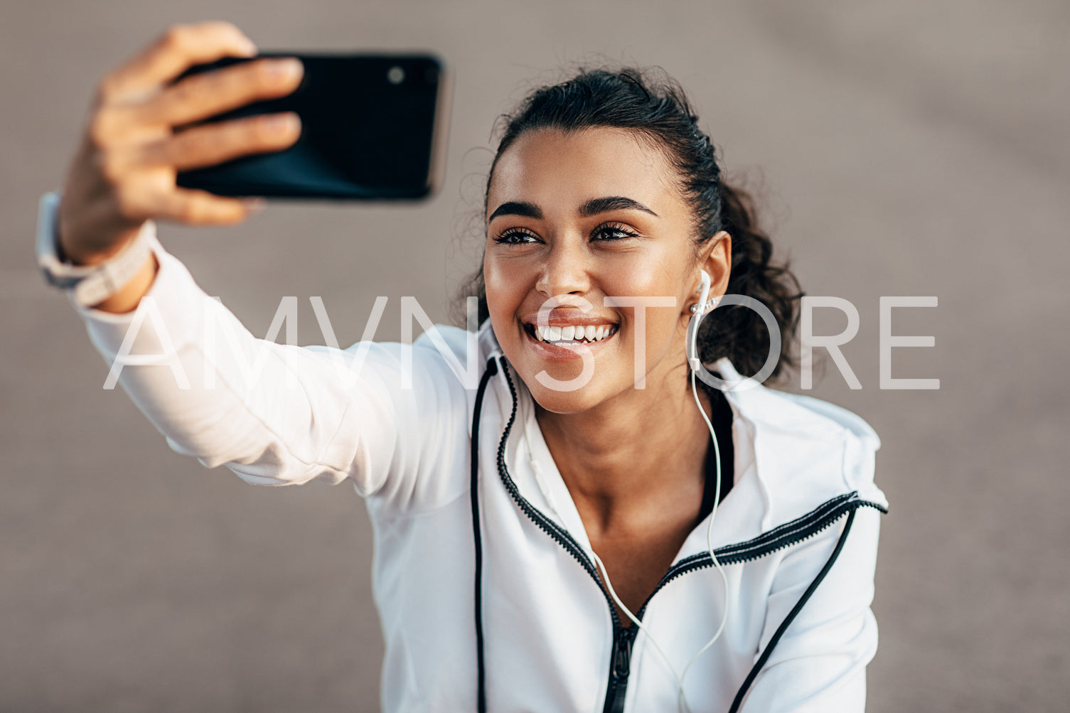 Happy woman sitting on city street wearing headphones and taking selfie after workout	