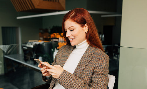 Redhead woman typing on smartphone while sitting at cafe