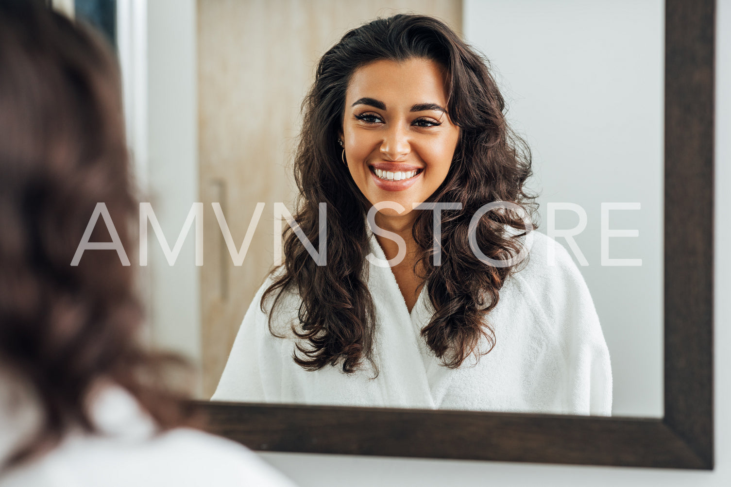 Portrait of a beautiful brunette woman wearing a white bathrobe and looking at her reflection in mirror	