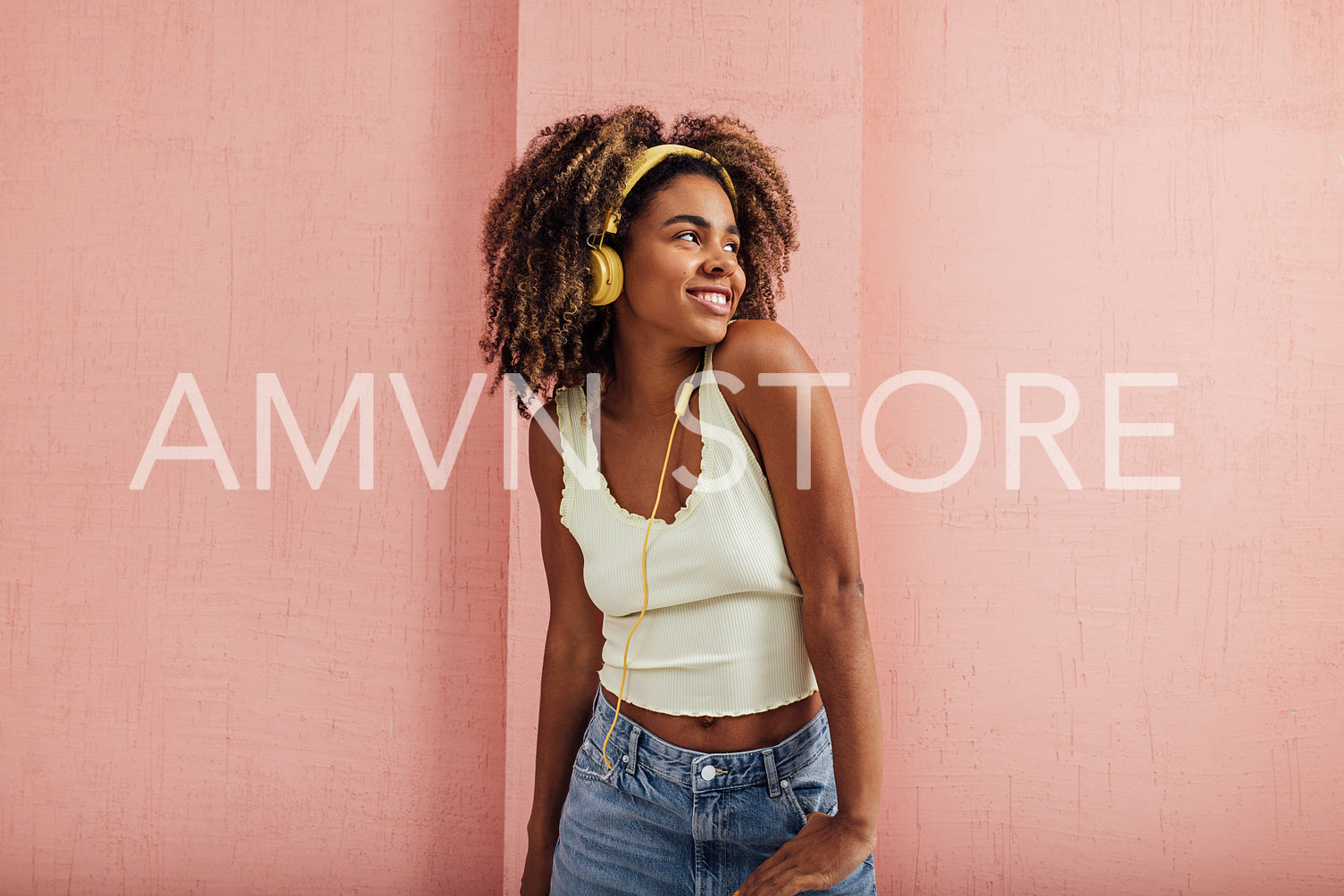 Woman wearing yellow headphones standing at pink wall looking aw