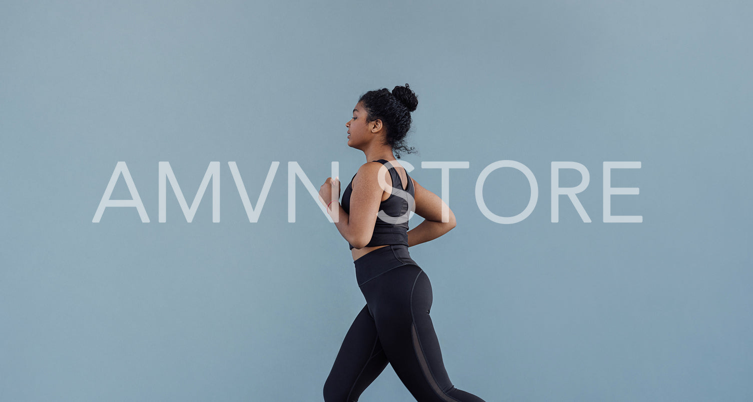 Side view of woman in black sportswear running at grey wall. Young female jogging outdoors.