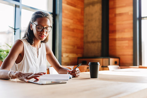 Woman at table browsing digital tablet while taking notes