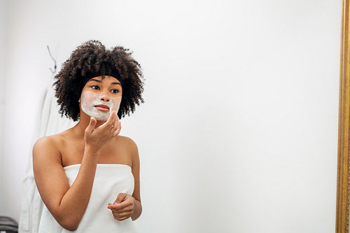 Woman applying facial mask in front of bathroom mirror