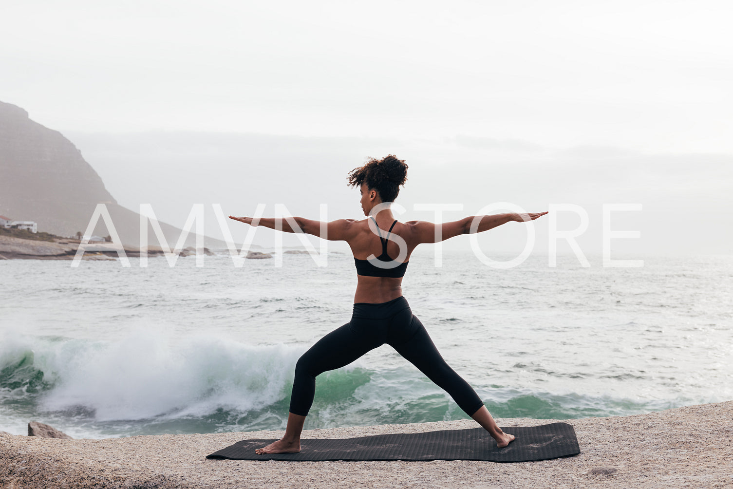 Back view of female practicing yoga in warrior pose by the ocean at bay