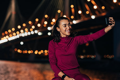 Sportswoman sitting outdoors at night taking a selfie against city lights