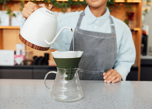 Unrecognizable barista pouring water into a filter with coffee