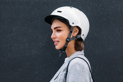 Side view of young woman wearing safety helmet. Female in scooter helmet standing at black wall.