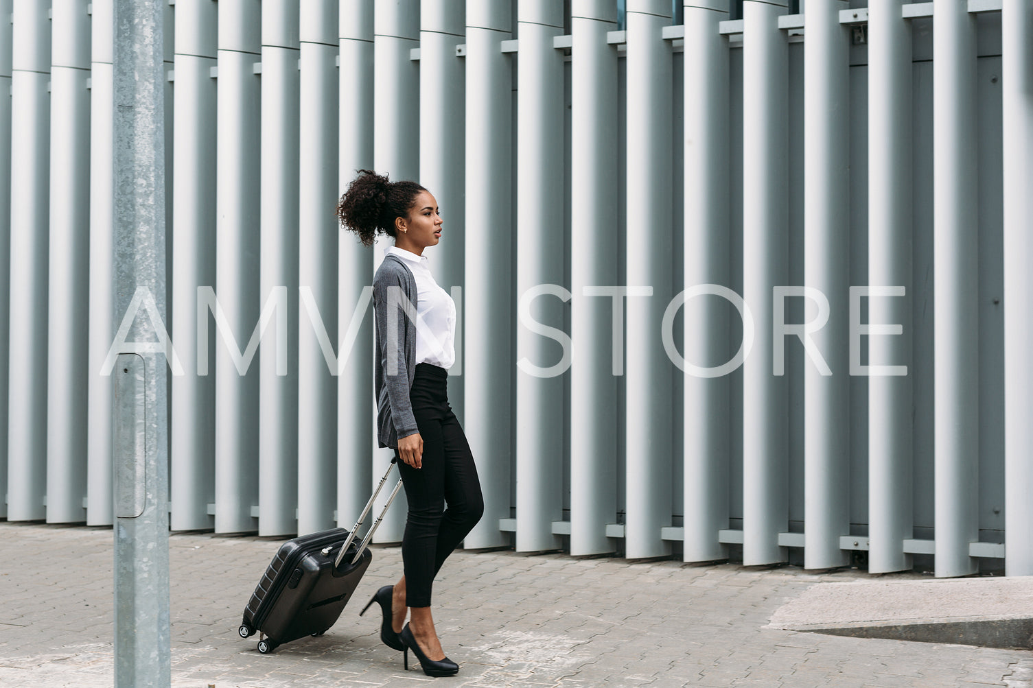 Businesswoman with rolling suitcase walking on street, side view	