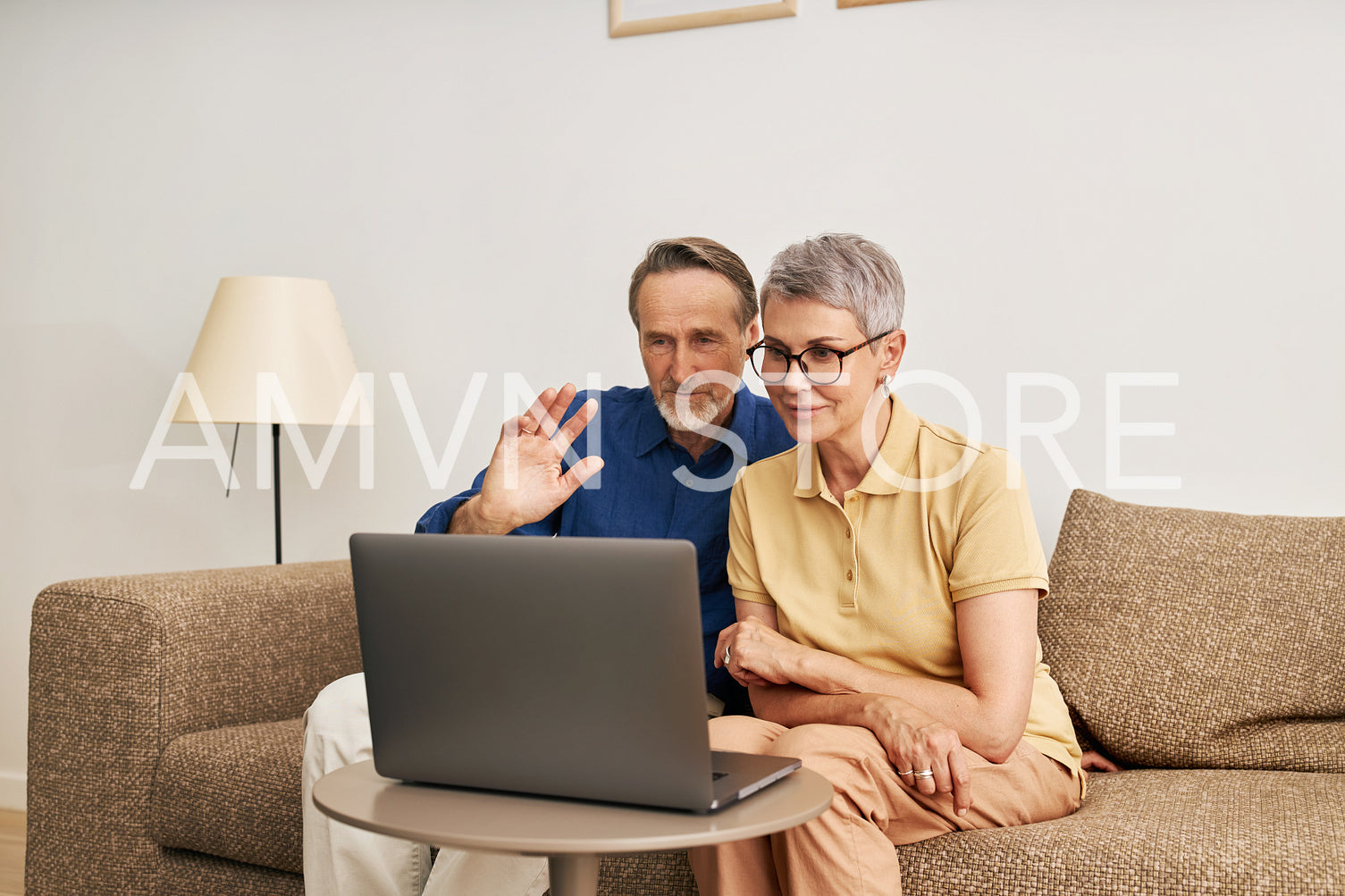 Happy senior couple waving while looking at laptop computer in home	