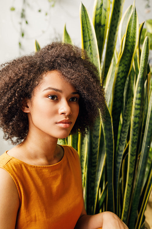 Portrait of beautiful young woman sitting near sansevieria leafs