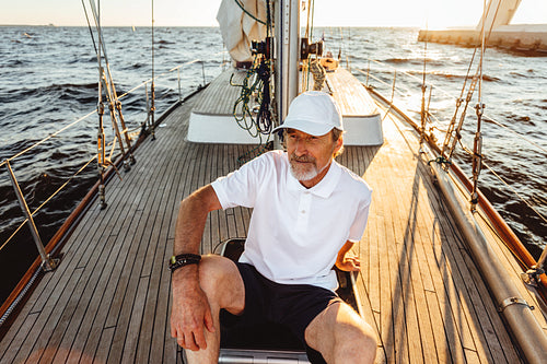 Senior man sitting on a deck of his yacht and enjoying sunset. Mature captain relaxing on sailboat.