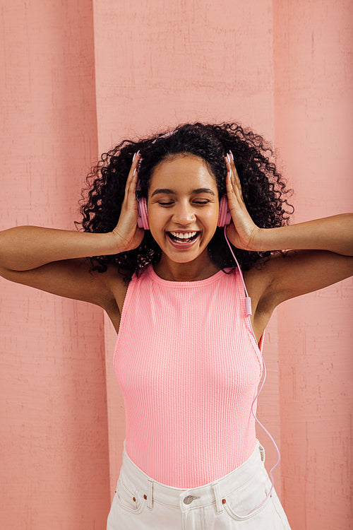 Laughing woman in bright casuals presses headphones with hands for better listening music