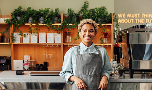 Confident coffee shop owner in an apron. Young smiling woman in an apron standing at the bar counter.