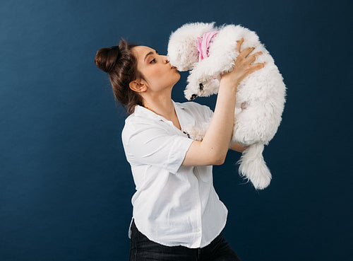 Side view of a woman holding and kissing her little white dog in