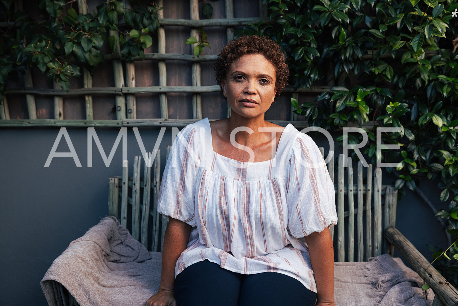 Portrait of a mature woman with short hair looking at camera while sitting on a bench at backyard of her house