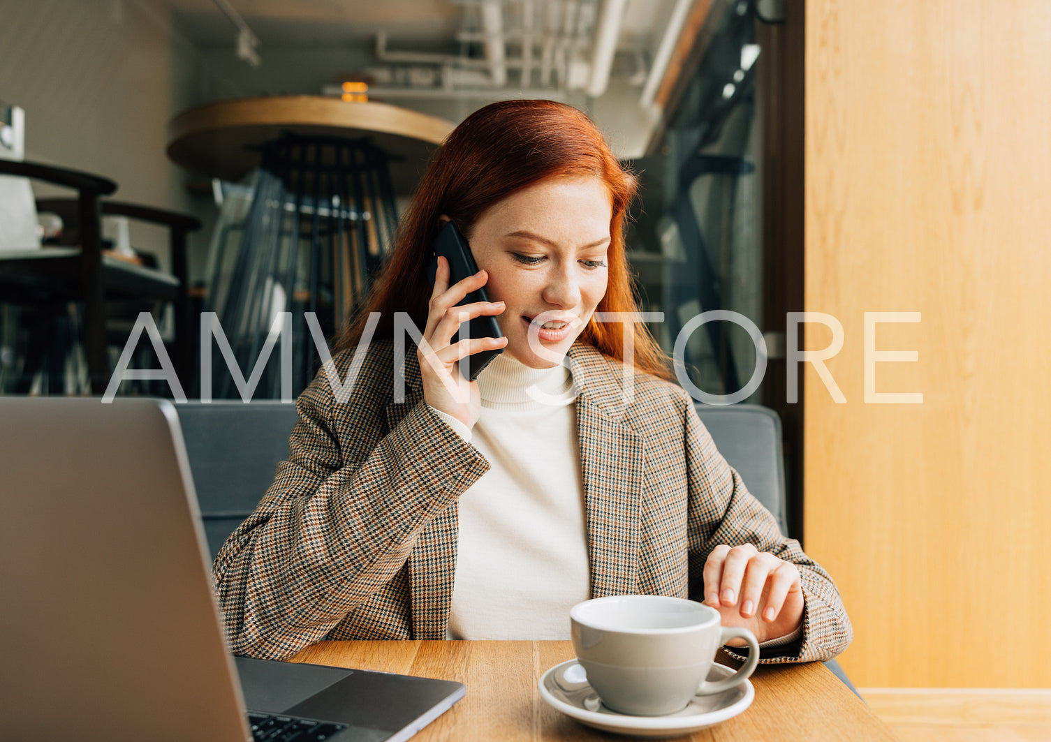 Young woman with ginger hair in formal wear talking on a mobile phone while sitting at a cafe