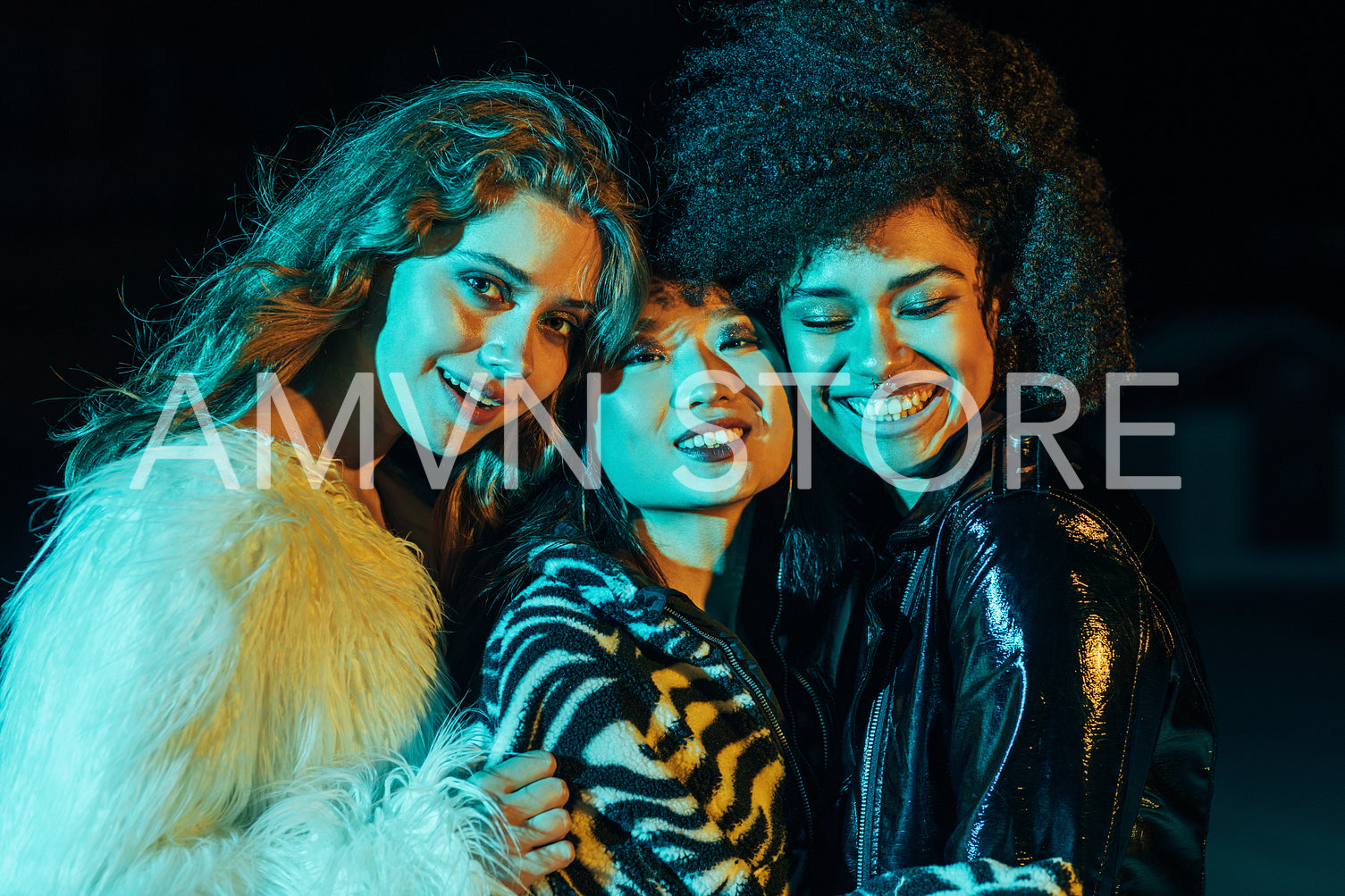 Close up of three happy girls looking at camera and embracing each other under colorful lights outdoors	