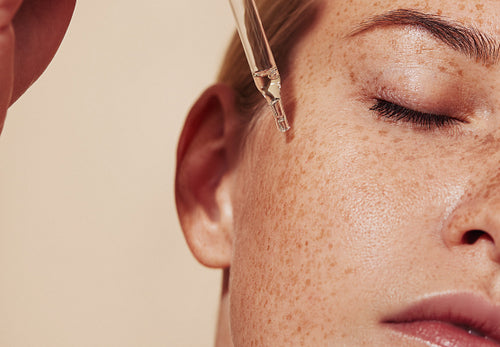 Close-up highly detailed shot of female skin with freckles and pipette with serum. Cropped shot of young woman with smooth perfect skin applying liquid serum on face.