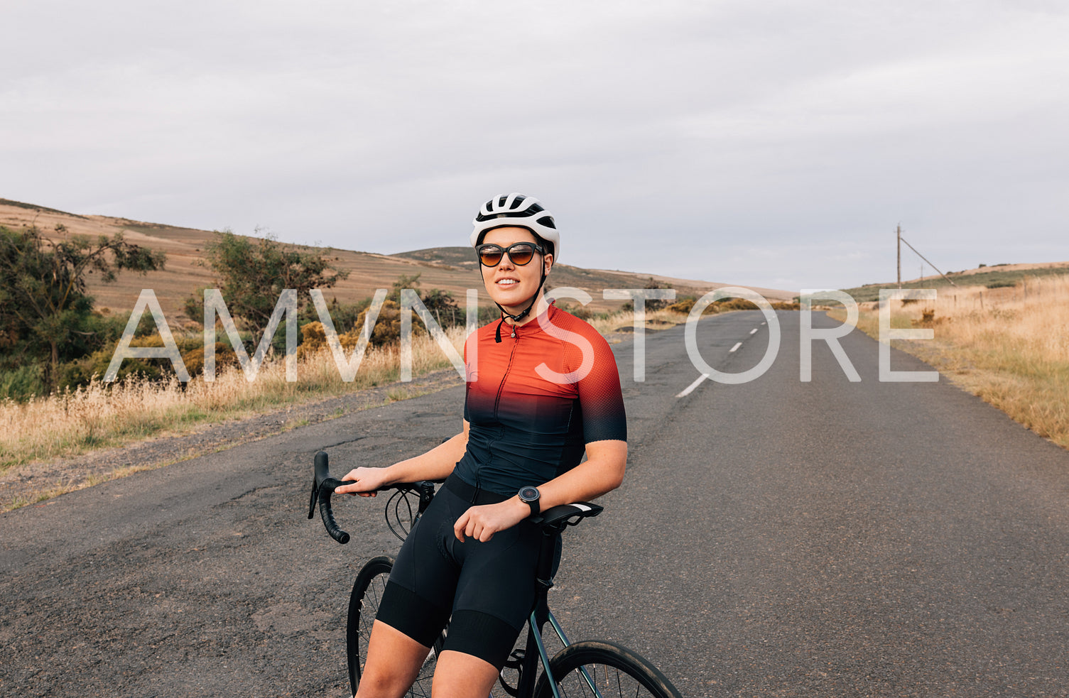 Professional woman cyclist in sunglasses and helmet sitting on bike relaxing after ride