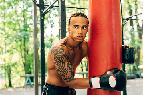 Man boxer leaning to rest on a punching bag at the sports ground