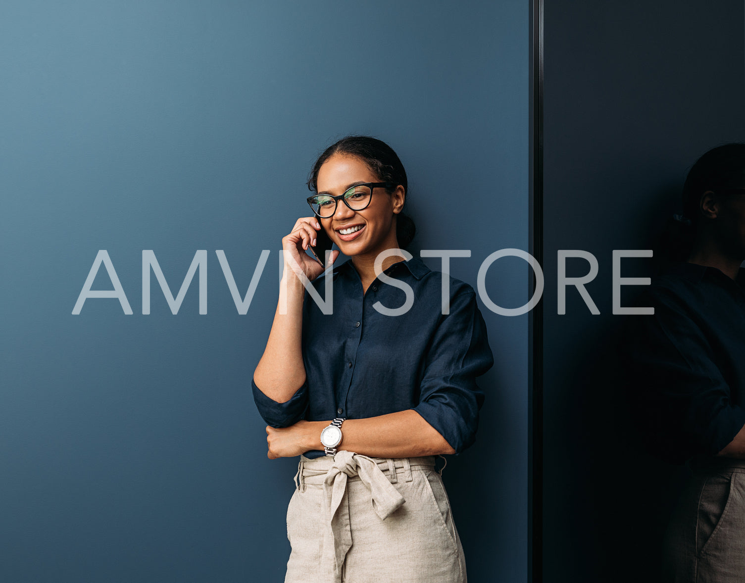 Smiling woman in formal clothes leaning blue wall talking on a mobile phone