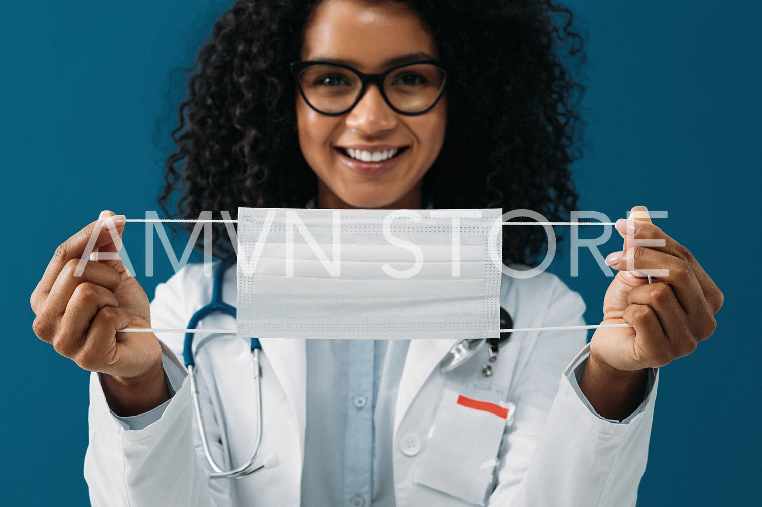 Close up of a female doctor holding a mask in her hands. Woman in medical uniform looking at camera at blue background.	