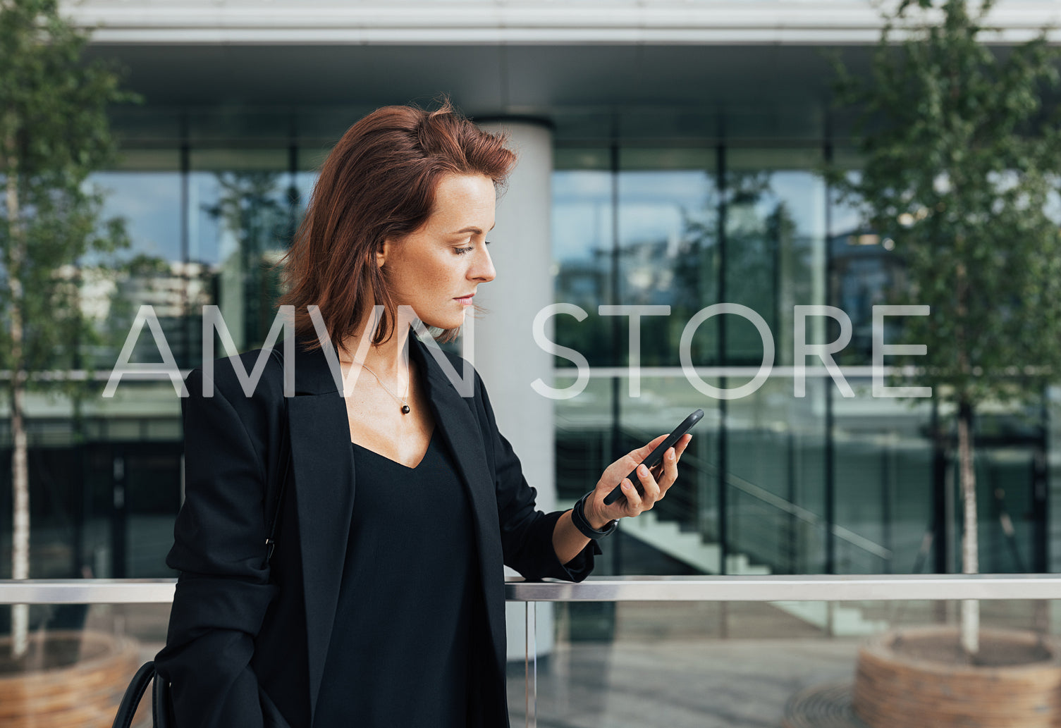 Side view of a confident businesswoman with ginger hair looking at her smartphone against an office building