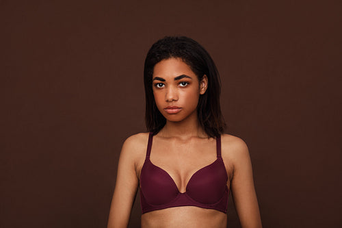 Portrait of a young woman with black hair against brown background. Young slim female in lingerie looking at camera in studio.