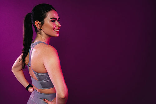 Rear view of young cheerful sportswoman looking away standing in studio at magenta background