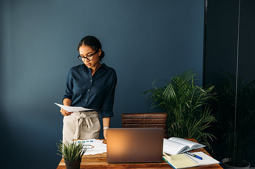 Young woman working from home standing at a desk and looking on documents