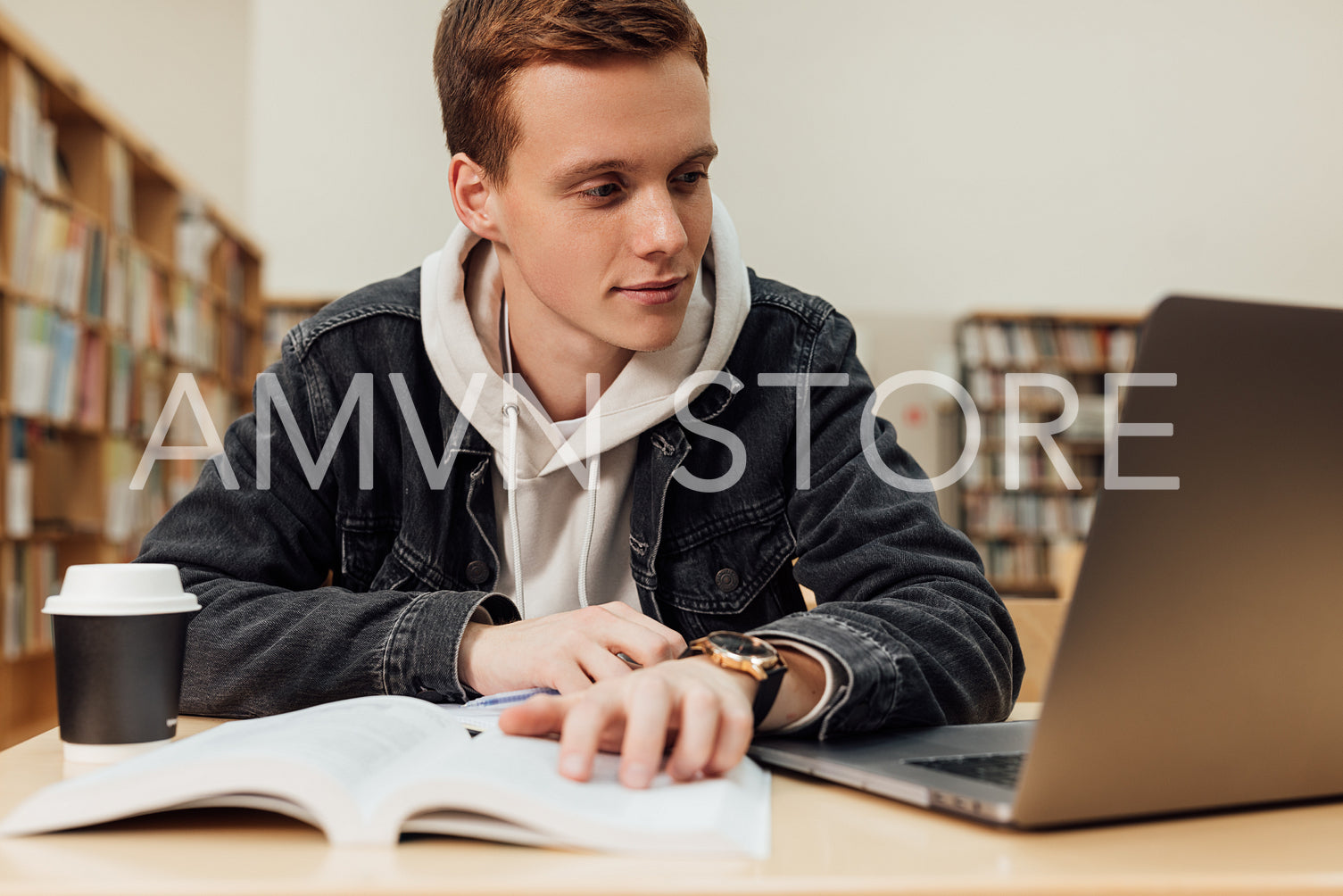 Male student sitting at desk looking at laptop. Young guy in library preparing exams.