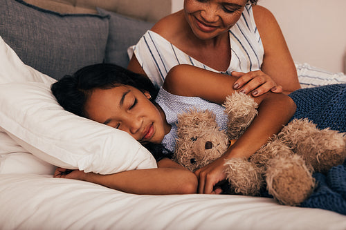 Smiling mature woman sitting near her granddaughter while she going to sleep