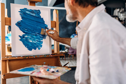 Inspired artist drawing an abstract picture in his workshop holding a palette