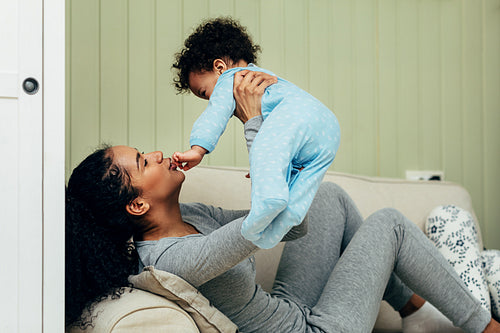 Side view of mother lifting baby in the air while lying on a sofa