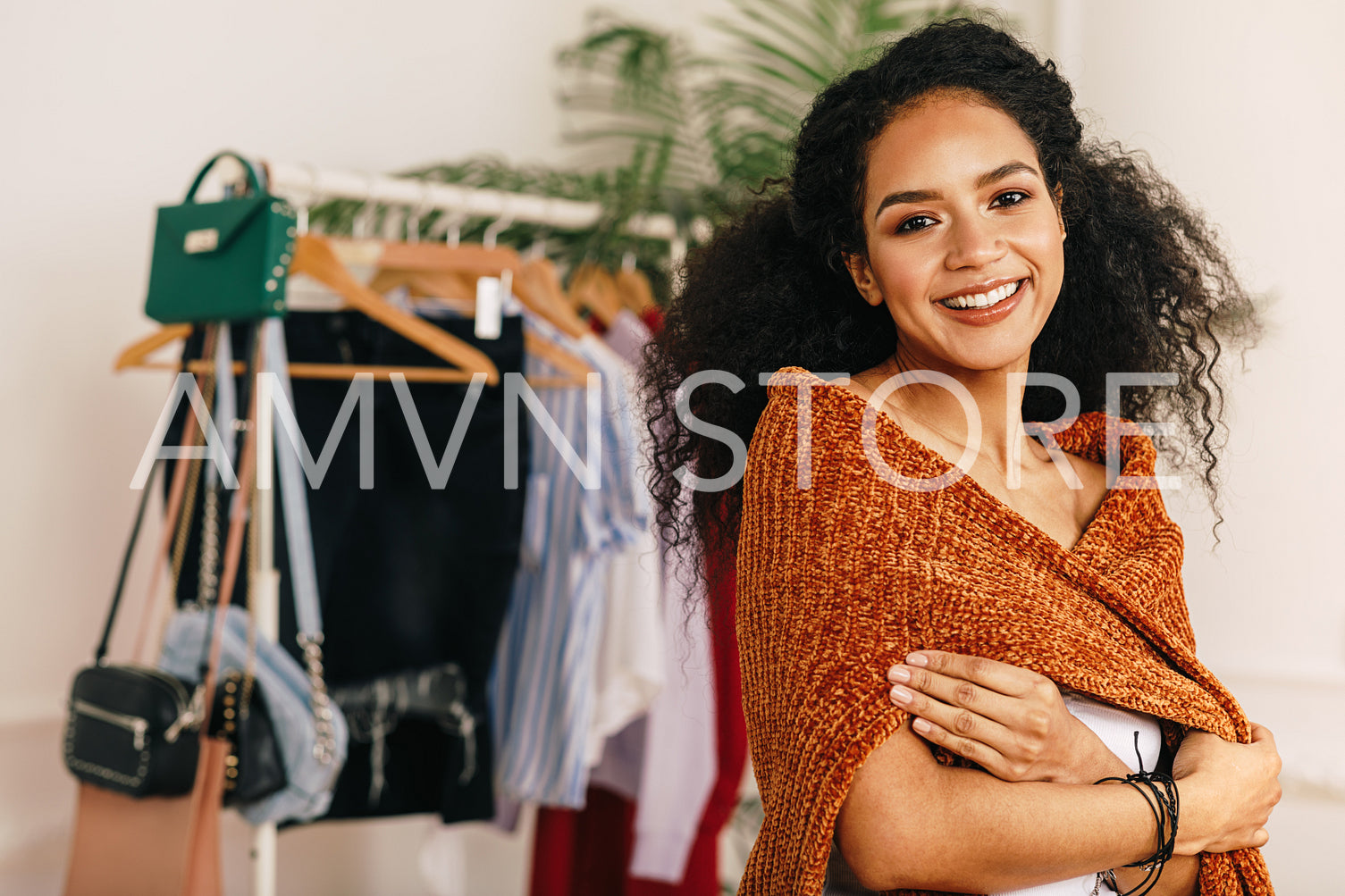 Portrait of a beautiful woman with curly hair standing at clothes rack	
