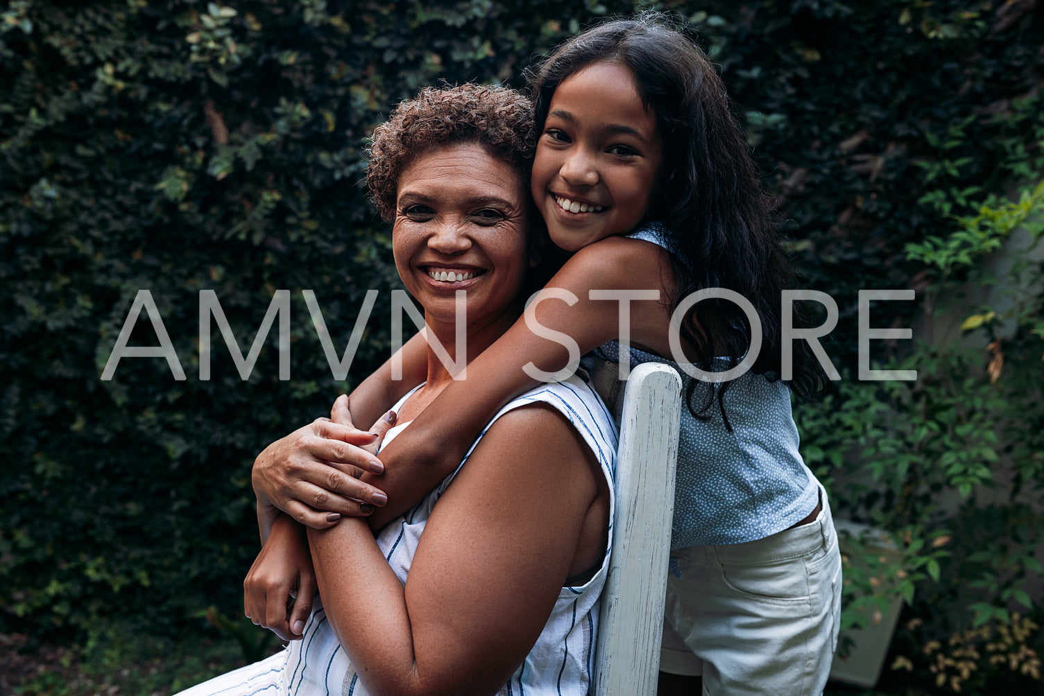 Smiling girl and her grandma looking at the camera. Grandmother and granddaughter hugging outdoors.