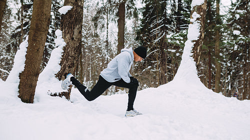 Runner doing stretching exercises in a snow forest