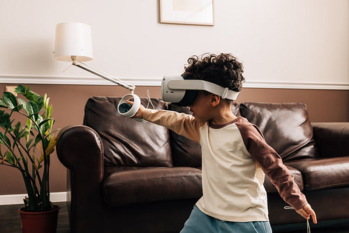 Little boy in VR goggles in living room. Kid enjoying virtual reality game using a controller.