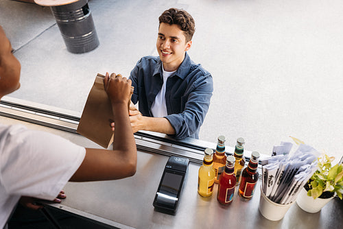 Young customer taking package with street food from an unrecognizable saleswoman at a food truck