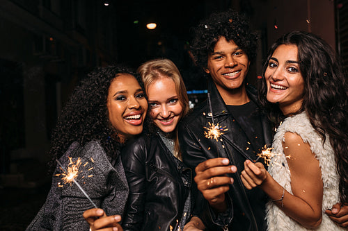 Group of young friends holding sparklers, looking at camera