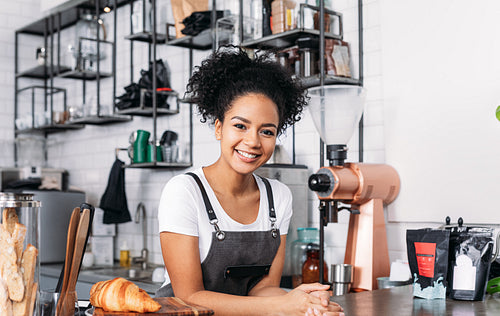 Beautiful female barista looking at camera. Cheerful waitress in an apron standing at a counter in a cafe.