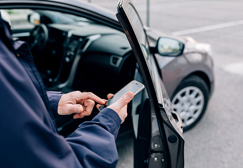 Male hands typing on cell phone. Unrecognizable mature man standing at rental car with smartphone.