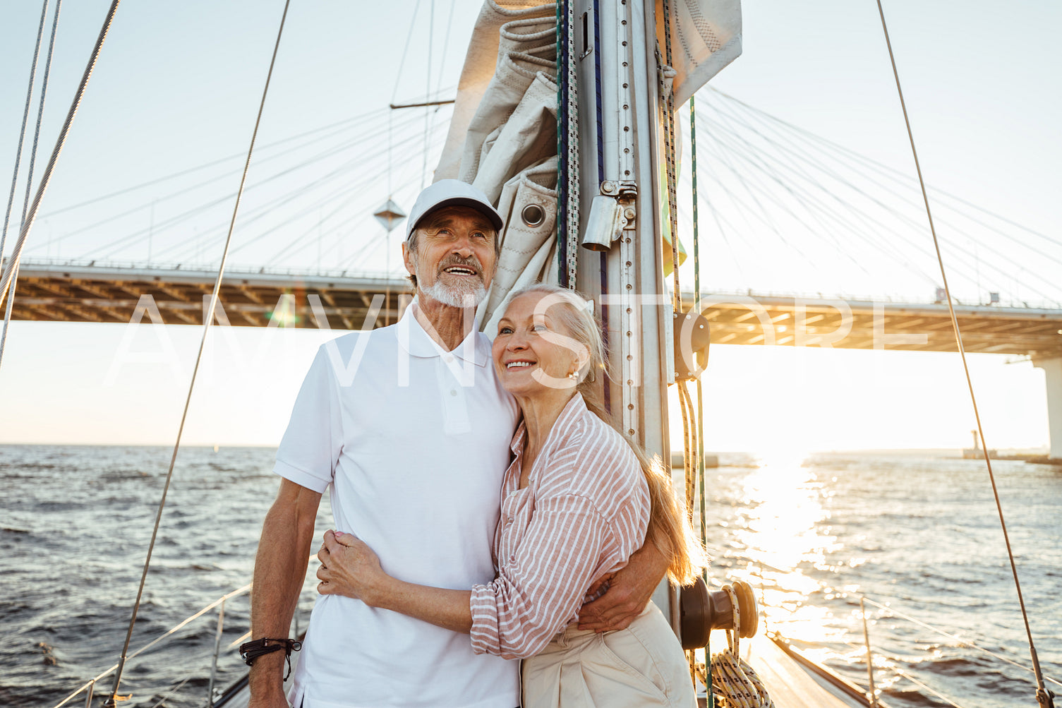 Happy mature couple embracing each other and looking away. Two people standing on sailboat and smiling.	