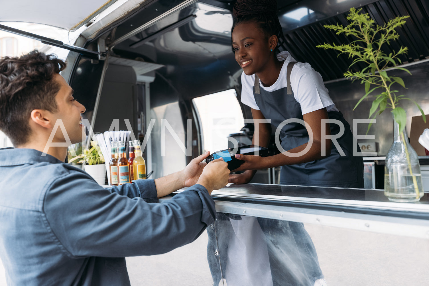 Young man with credit card paying to a saleswoman at a food truck. Female entrepreneur in apron receiving payment from a customer.