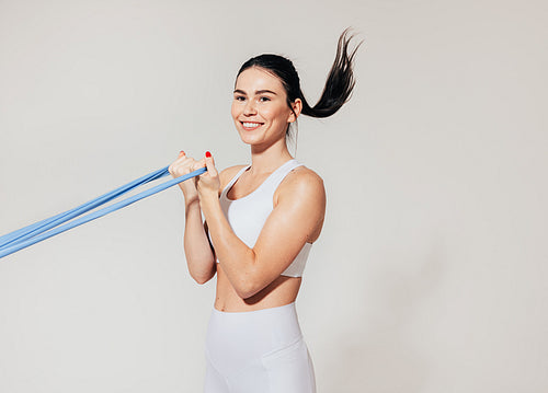 Smiling woman doing biceps curl with resistance band at white wall