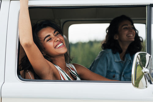 Young laughing woman putting her hand out of a car having fun during road trip