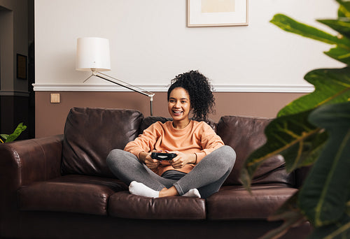 Cheerful female with joystick sitting on sofa playing video game while entertaining at home