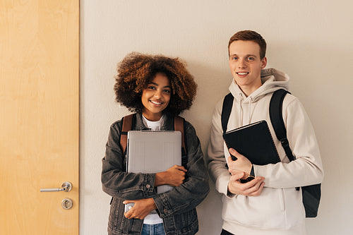 Two classmates standing at wall. Boy and girl in casuals with backpacks looking at camera.